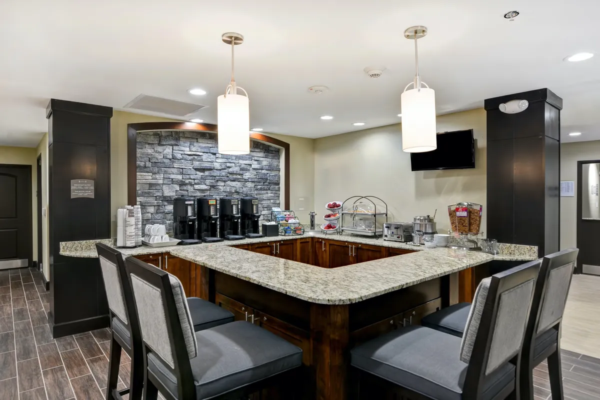 The image depicts a granite countertop with a coffee station set against a stone feature wall, complemented by a cozy seating area. The scene evokes a relaxed morning or afternoon atmosphere for socializing or unwinding.