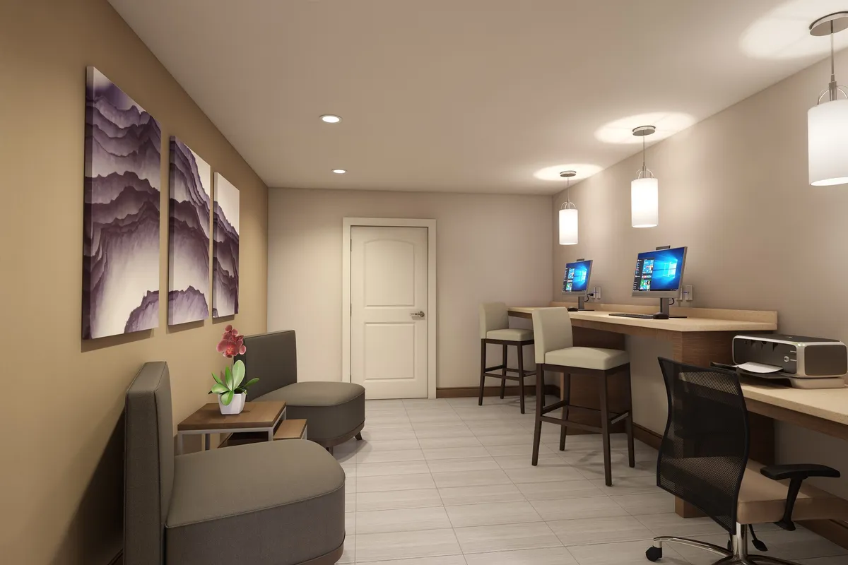 This image features a business center with several computer stations, comfortable seating, and tasteful artwork on the wall. The space is functional yet welcoming, providing a productive environment for guests who need to work or hold casual meetings.