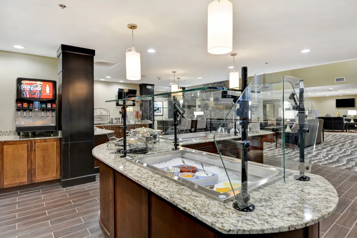 This interior image features a buffet area with a Coca-Cola dispenser, modern decorative lighting, and a well-arranged seating area. The space looks casual and inviting for families to enjoy meals together.