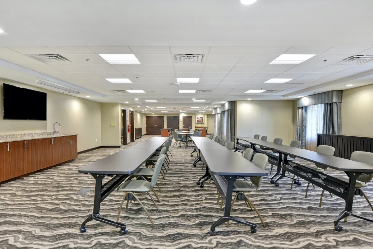 A modern meeting room set up with long tables arranged in a U-shape, comfortable chairs, a large TV screen, and a bar area. The mood is productive and professional, suitable for business meetings, workshops, or networking events.